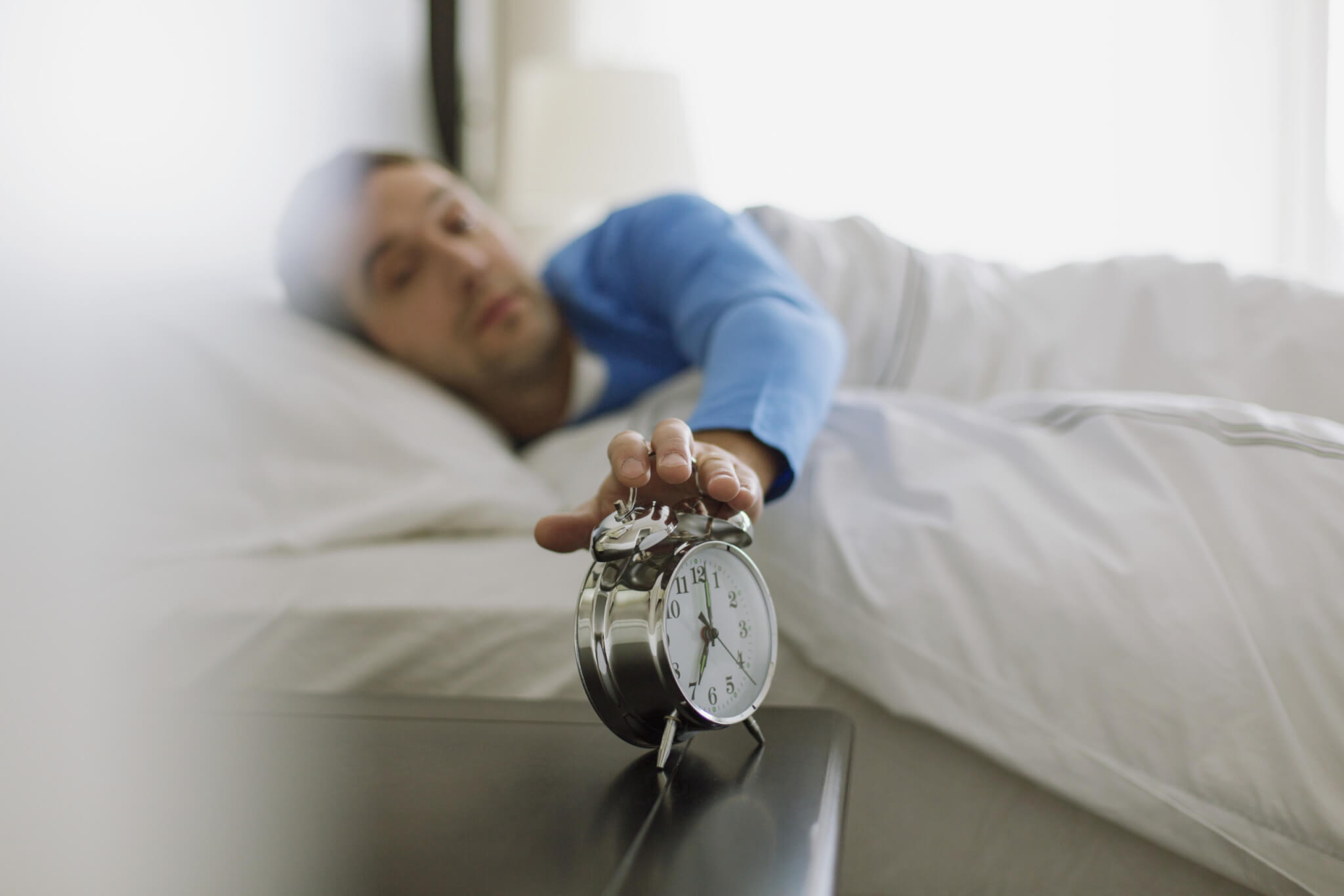Man reaching for snooze button on alarm clock